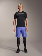 Alpinestars A-Aria Switch Jersey, Short Sleeve MTB Jersey, Black with mirrored white Alpinestars logo, worn by a male model with blue cycling shorts and black knee pads, breathable performance apparel for trail riding