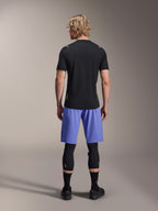 Male rider wearing Alpinestars A-Aria Lite Shorts, MTB Shorts, Baja Blue, back view, styled with a black short-sleeve jersey, black knee guards, and black cycling shoes, performance mountain biking apparel