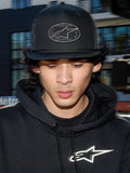 Alpinestars Contender Trucker Hat, black lifestyle cap with poly mesh back, structured crown featuring an embroidered Astars logo patch, worn by a man with a black Alpinestars hoodie, casual motorsport-inspired streetwear.