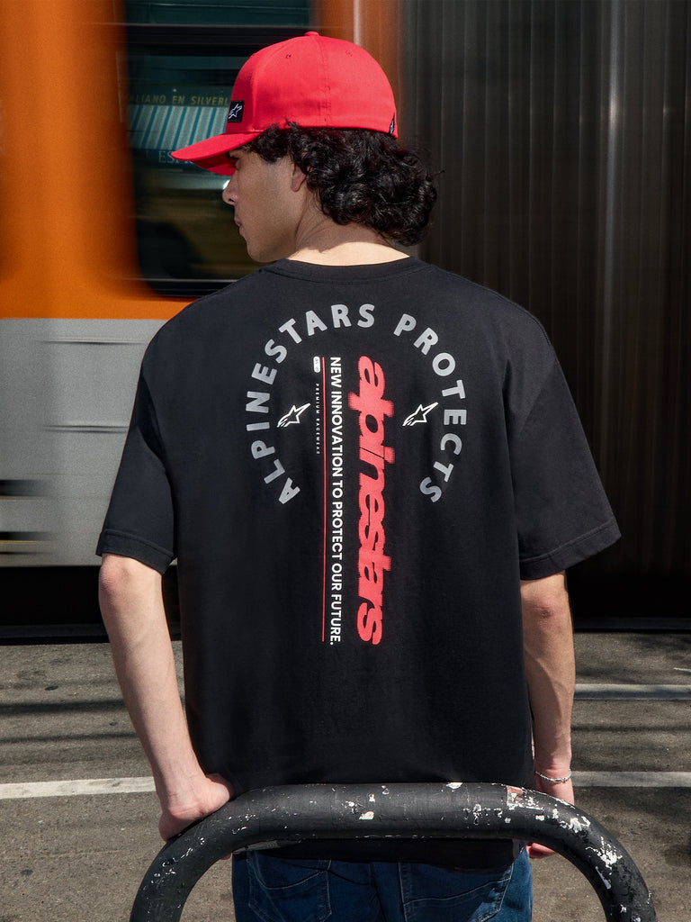 Alpinestars Overhang Oversized CSF Tee, Black Short Sleeve T-Shirt, back view featuring vertical red wordmark and circular Alpinestars Protects graphic, worn with a red cap, casual motorsport streetwear