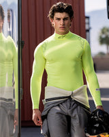 Alpinestars ZX Evo V3 Top - Long Sleeve, Auto Racing Base Layer, Yellow Fluo, worn by a male driver with a grey racing suit tied around his waist, holding a black helmet, featuring Alpinestars logo on the neck and shoulders, technical moisture-wicking gear for motorsport
