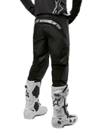 Alpinestars 2024 Fluid Graphite Pants, Motocross Pants, Black and Silver, rear view showing silver Alpinestars branding on the back yoke, worn with white and black motocross boots, durable textile design for off-road riding