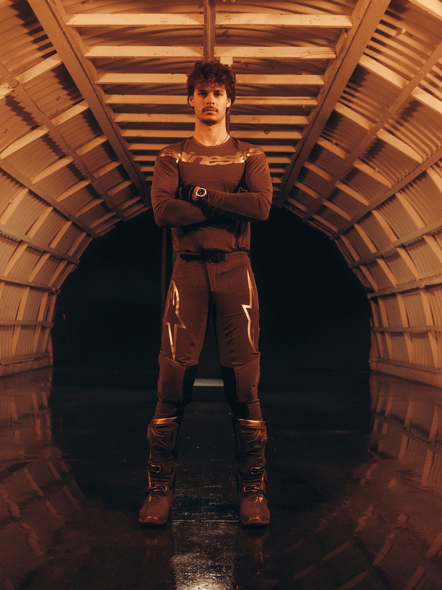 Alpinestars Limited Edition Supertech Air Gold Jersey, men's motocross gear, brown and gold, worn in an arched tunnel.