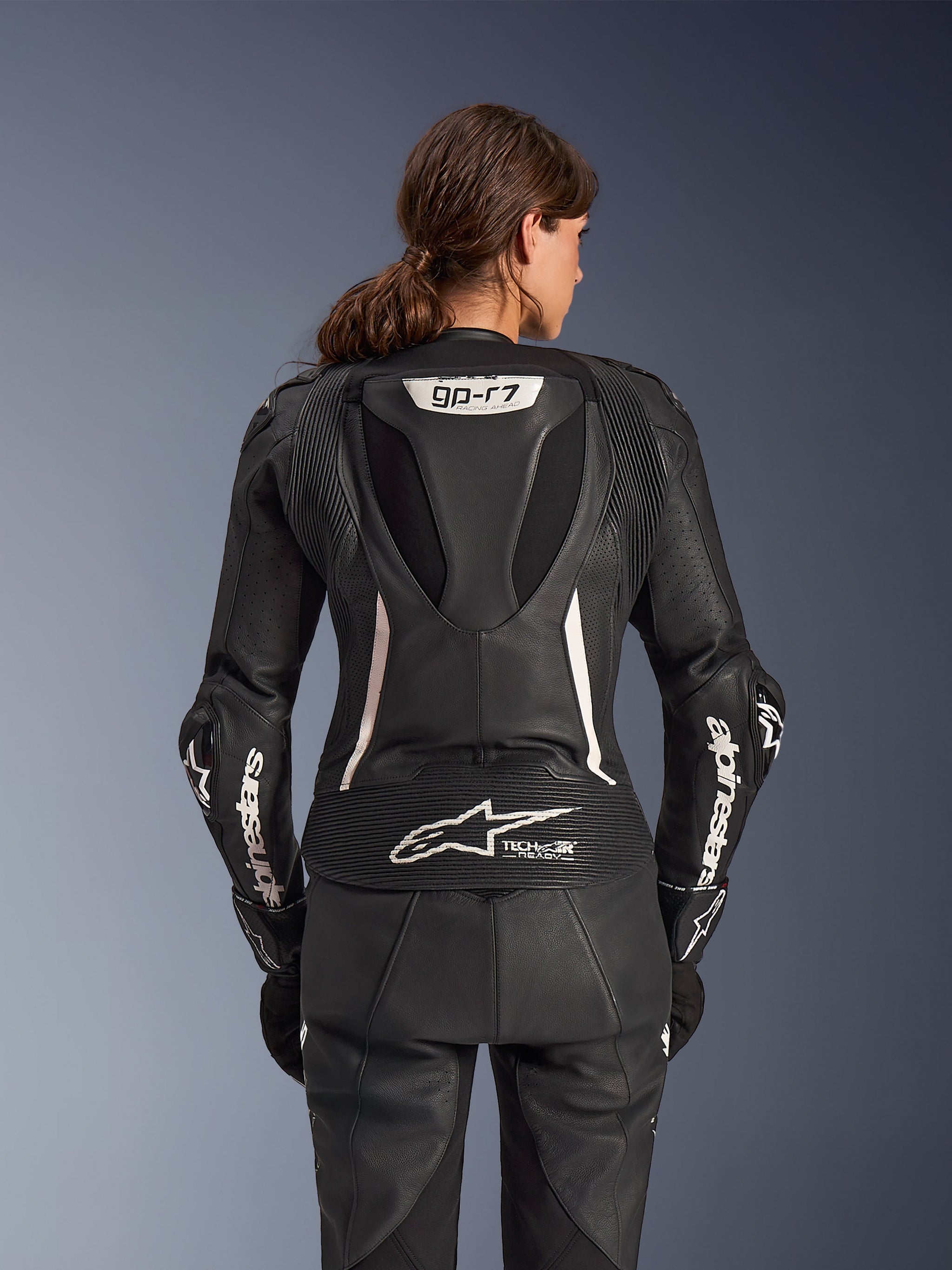 Alpinestars Stella GP-R7 2-Piece Leather Suit, Women's Motorcycle Suit, Black with white accents, back view showing the Supertech R10 aero hump with GP-R7 logo, Tech-Air Ready branding on the lower back, white Alpinestars lettering on the sleeves, and accordion stretch panels for racing performance