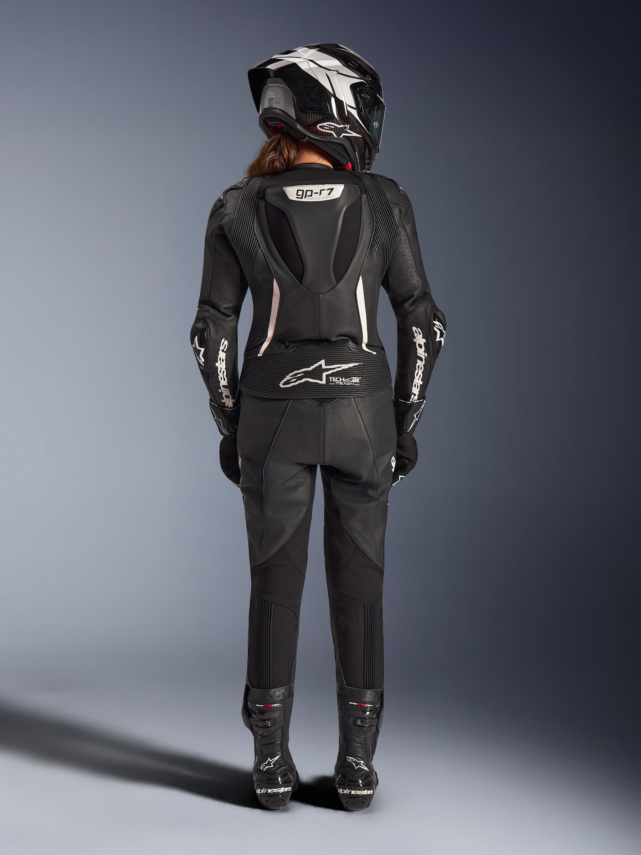 Alpinestars Woman Stella GP-R7 2-Piece Leather Suit, Black with white accents, Rear view showing Supertech R10 aero hump and Tech-Air Ready logo, worn with matching full-face helmet, racing gloves, and leather boots for track and sport riding