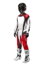 Motocross rider wearing full Alpinestars gear, 2024 Techstar Ocuri Pants in Mars Red White Black, matching jersey, black helmet with goggles, black and white gloves, and white motocross boots, professional off-road racing outfit