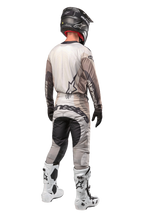 Alpinestars 2024 Techstar Pneuma Pants, Motocross Pants, Dark Sand and Iron Dust Gray, back view worn by a rider with a matching jersey, white and black boots, and a black helmet, featuring bold Alpinestars branding on the seat and reinforced dark panels