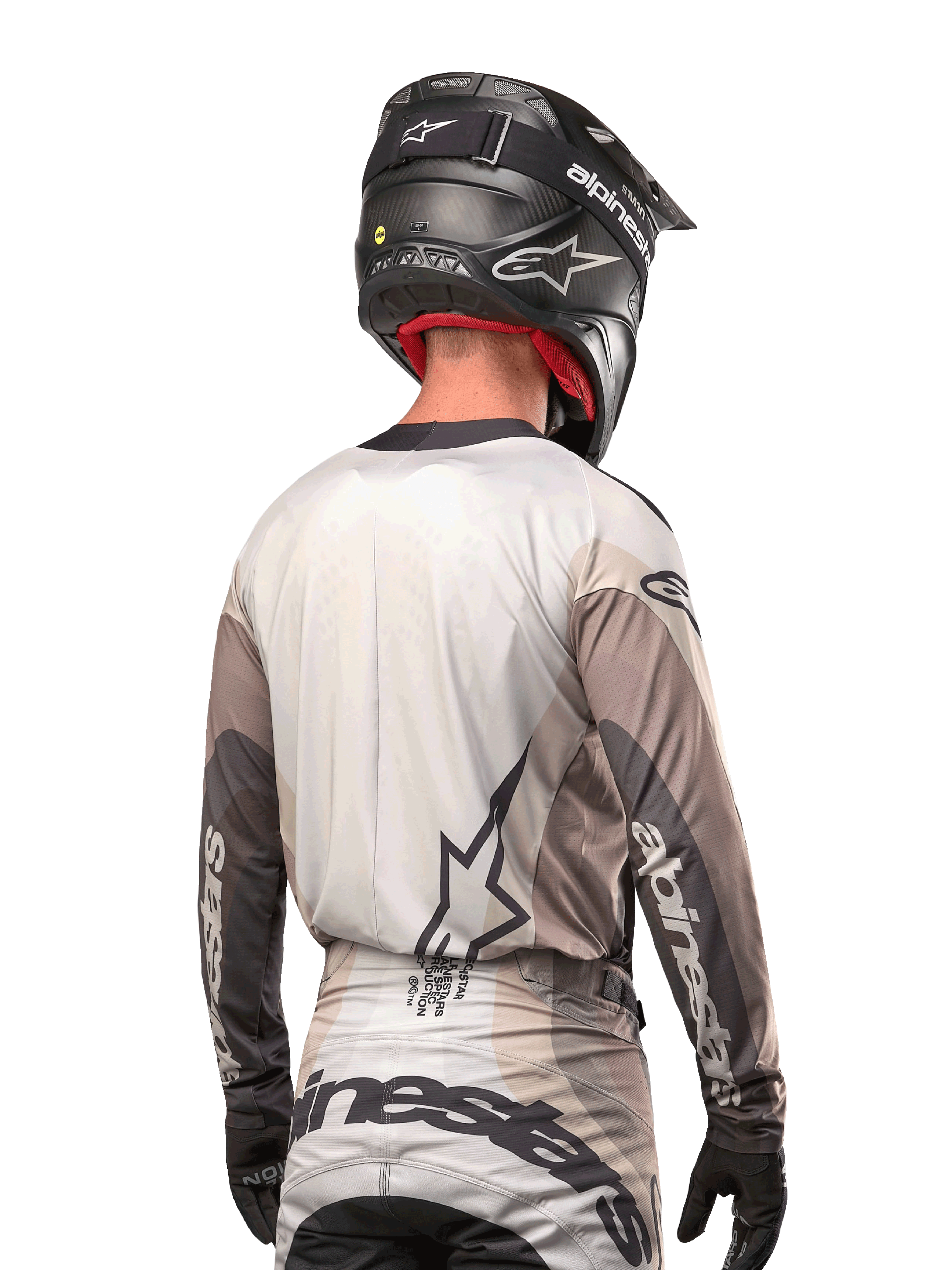 Motocross rider from behind wearing the Alpinestars 2024 Techstar Pneuma Jersey in Dark Sand Iron Dust Gray, paired with a black carbon-finish helmet, featuring a large star logo on the back and Alpinestars branding on the sleeves.