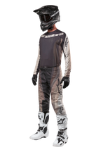 Alpinestars 2024 Techstar Pneuma Pants, Motocross Pants, Dark Sand Iron Dust Gray, worn as part of a complete gear set with matching jersey, black helmet, black gloves, and white boots, featuring tonal desert camo patterns with large logo accents