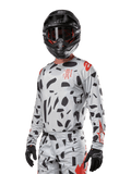 Alpinestars 2024 Techstar Rantera Jersey, Motocross Jersey, Haze Gray Camo with black abstract patterns and red accents, long-sleeve design worn with matching black helmet and gloves, technical off-road racing gear