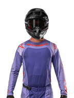 Alpinestars 2024 Techstar Ocuri Jersey, Purple and Hot Orange, worn by a motocross rider with a black helmet and goggles, featuring laser-cut perforations on the chest, athletic race fit, and bold red branding on the shoulders and chest.