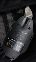 Alpinestars Tech-Air 3 V2 System, Internal view of the gas inflator and ECU housing, black plastic with embossed logo, safety label with QR code and installation diagrams, black mesh interior lining, detail of the user-serviceable autonomous airbag system